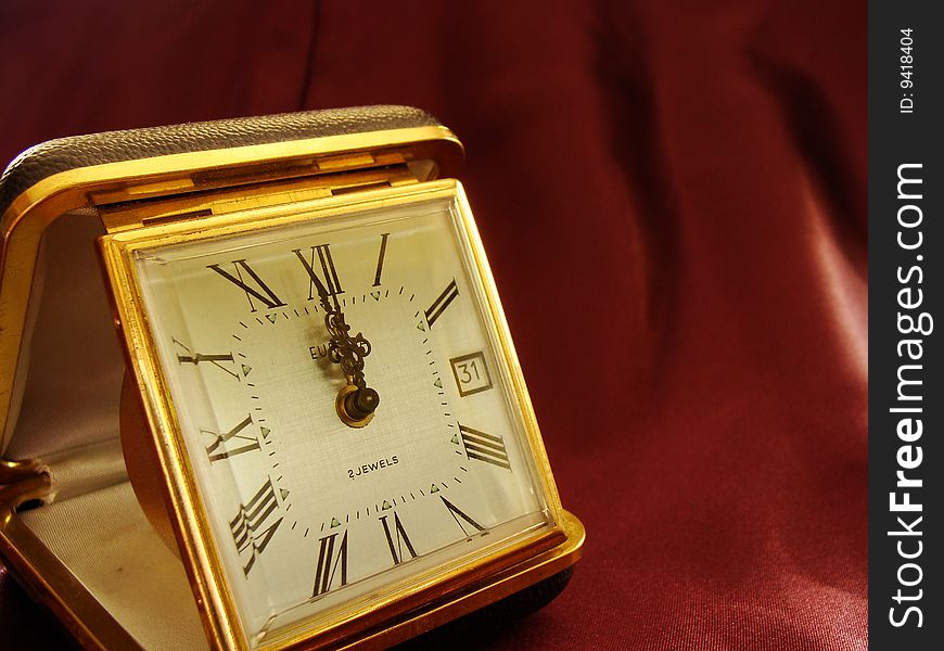 Concept of time measuring, golden clock on dark red fabric background