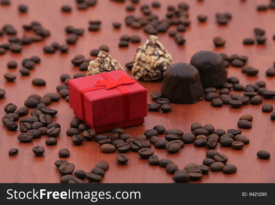 On a wooden table the red gift box and tasty chocolates lies. On a table coffee grains are scattered. On a wooden table the red gift box and tasty chocolates lies. On a table coffee grains are scattered