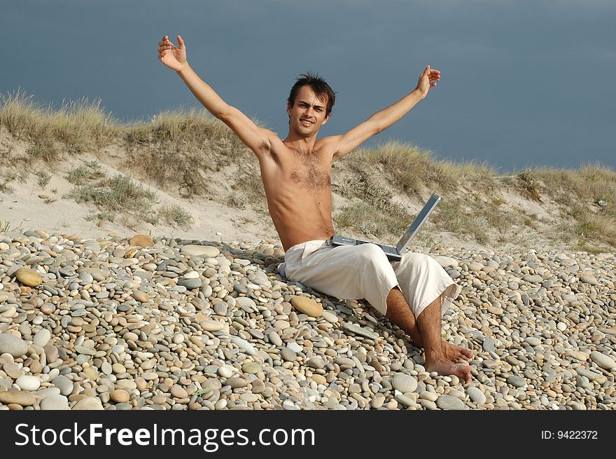 Handsome young with computer on the beach without a t-shirt. Handsome young with computer on the beach without a t-shirt