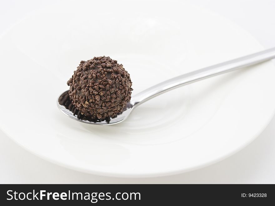 Chocolate truffle on a silver spoon and white plate isolated on white background