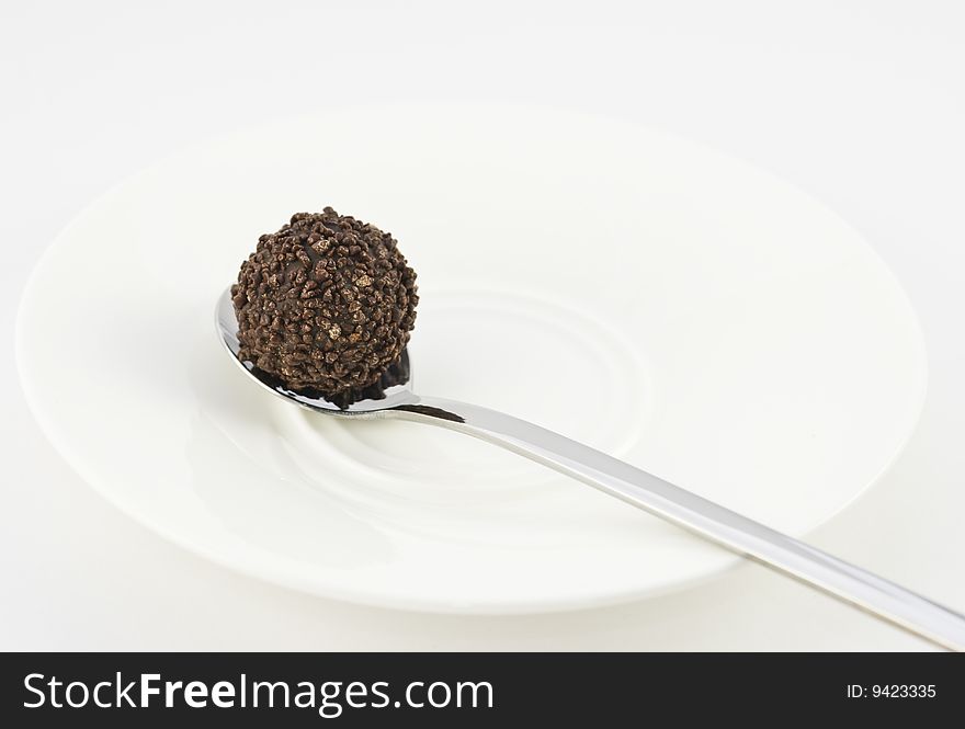 Chocolate truffle on a silver spoon and white plate isolated on white background