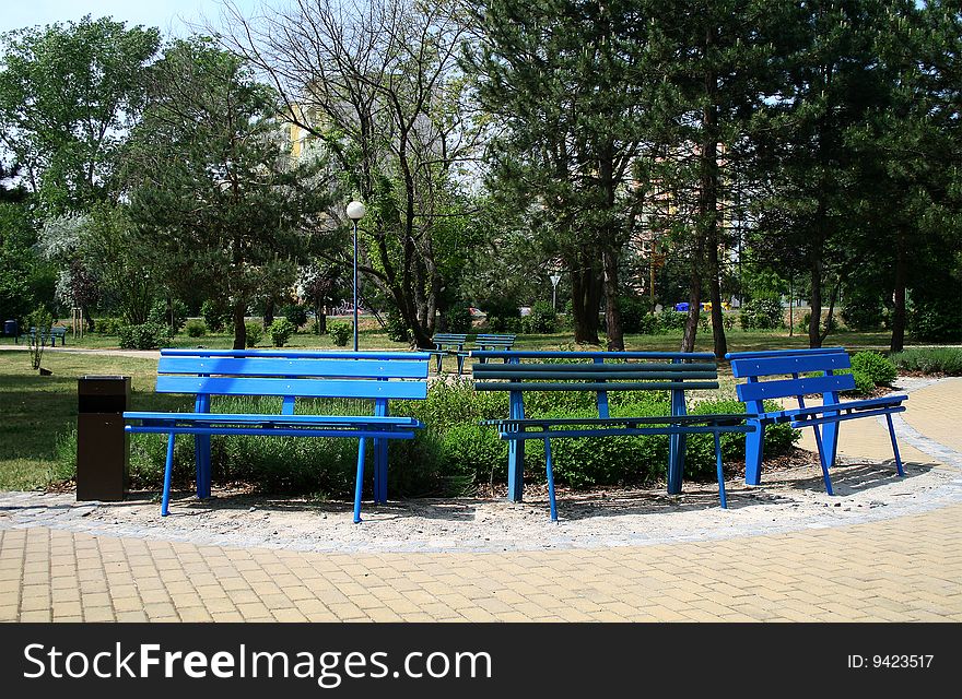 Three blue benches in the park. Nature in the background.