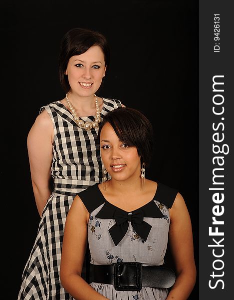 A portrait of two beautiful woman in dresses, on black studio background. A portrait of two beautiful woman in dresses, on black studio background.