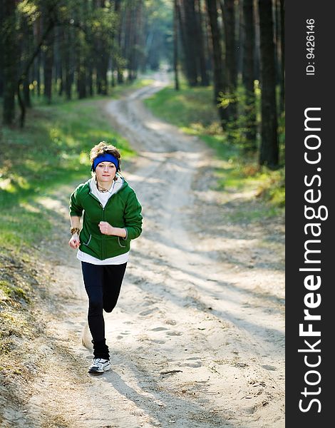 Pretty young girl runner in the forest while listening to music.