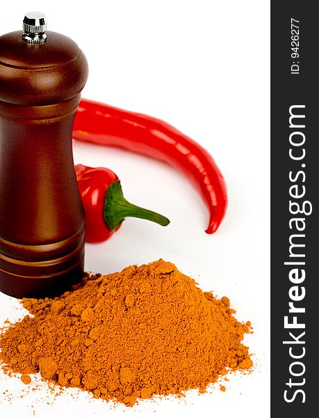A composition of two pods of red hot pepper , a wooden hand mill for grinding and a little of ground pepper on a white background. A composition of two pods of red hot pepper , a wooden hand mill for grinding and a little of ground pepper on a white background