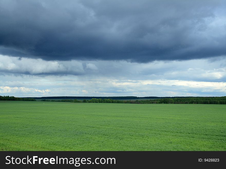Panoramic landscape with green field under storm clouds
