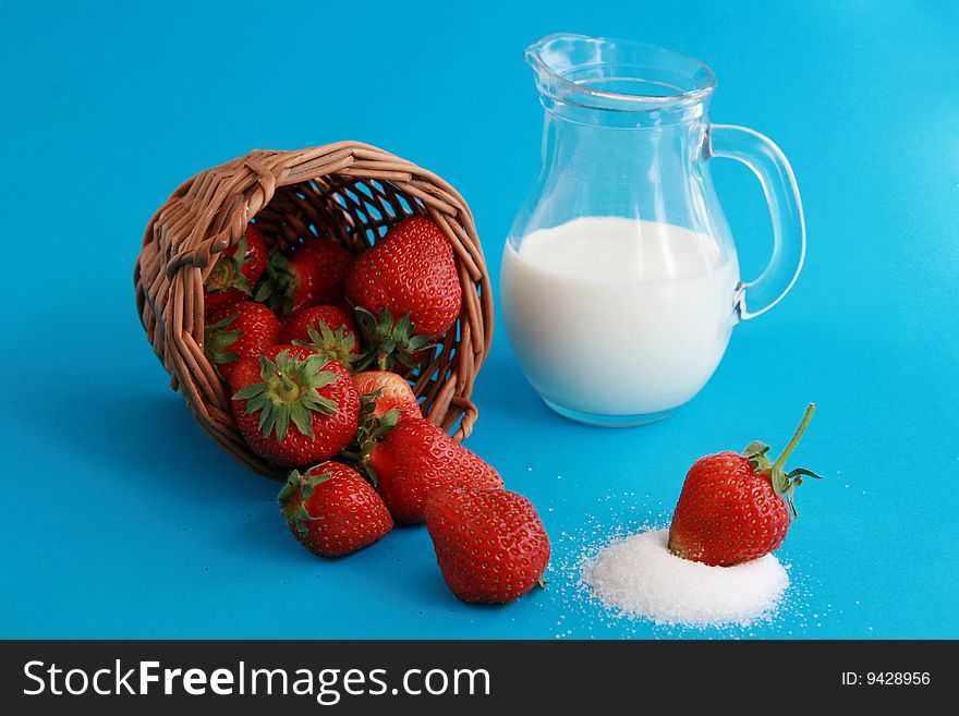 Strawberries in a wicker basket, jug of milk or yoghurt and sugar on blue background. Strawberries in a wicker basket, jug of milk or yoghurt and sugar on blue background.