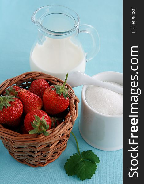 Strawberries in a wicker basket, jug of milk or yoghurt and sugar on blue background. Strawberries in a wicker basket, jug of milk or yoghurt and sugar on blue background.