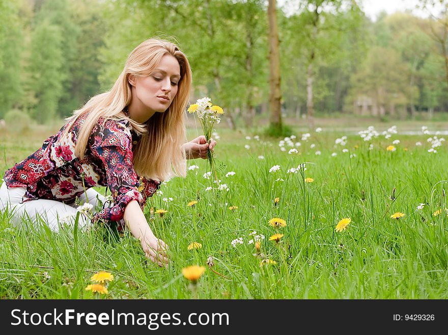 Young blond girl collecting flowers in the grass