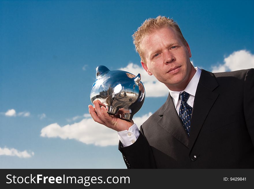 A businessman holds a piggy bank up to his ear. A businessman holds a piggy bank up to his ear