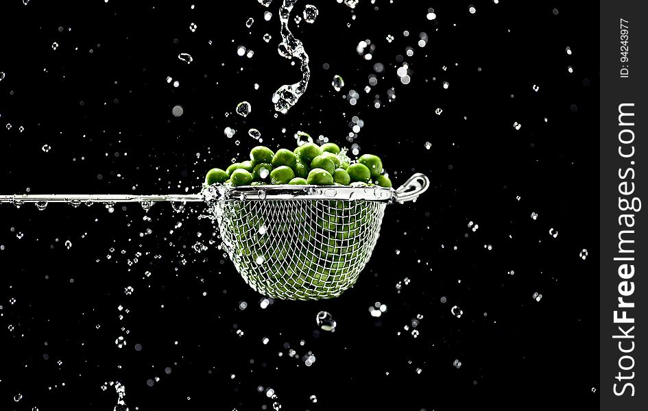 A close up of peas in a metal strainer and water drops around it. A close up of peas in a metal strainer and water drops around it.
