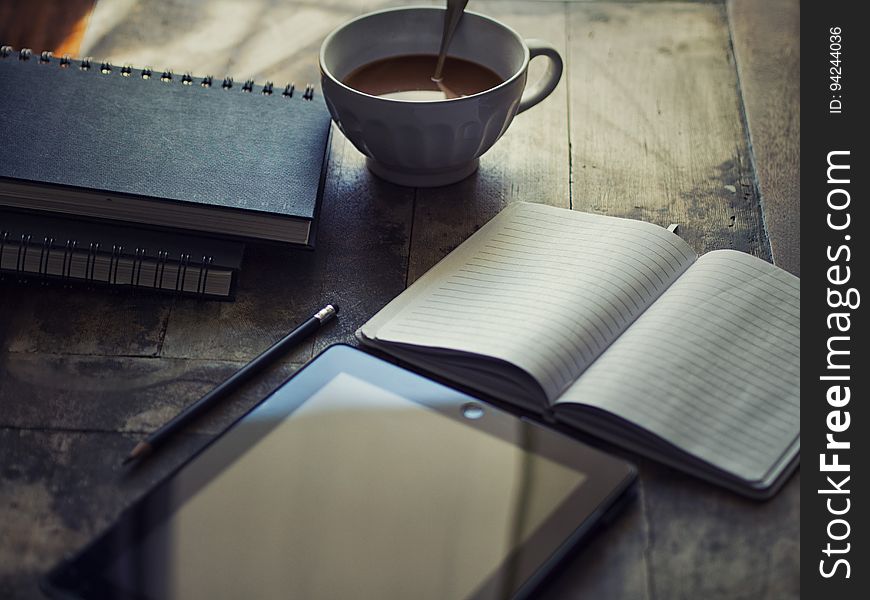 Still life with tablet or e-reader on rustic table with blank journal and cup of coffee. Still life with tablet or e-reader on rustic table with blank journal and cup of coffee.