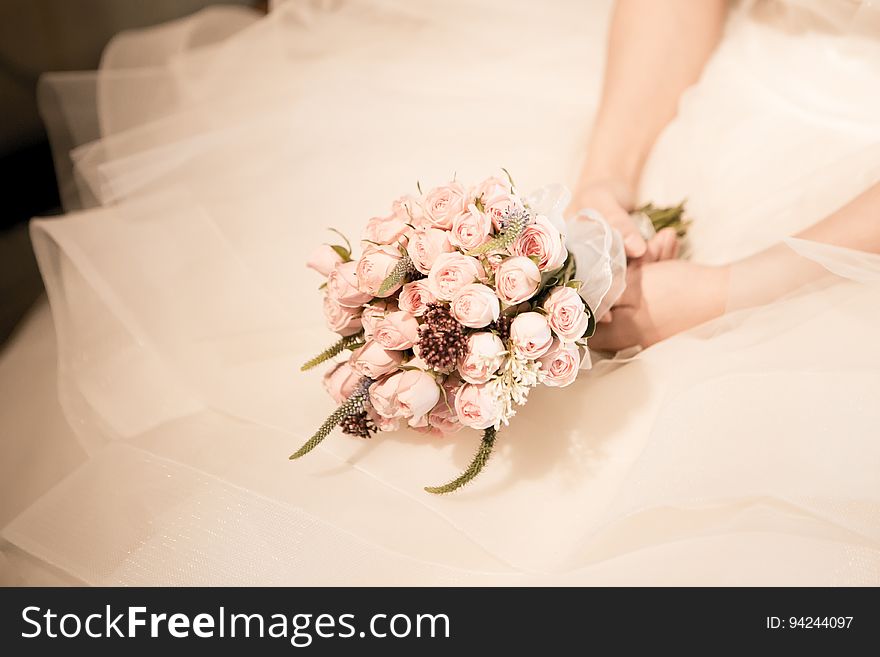 Close up of bride holding bouquet over folds of white gown. Close up of bride holding bouquet over folds of white gown.