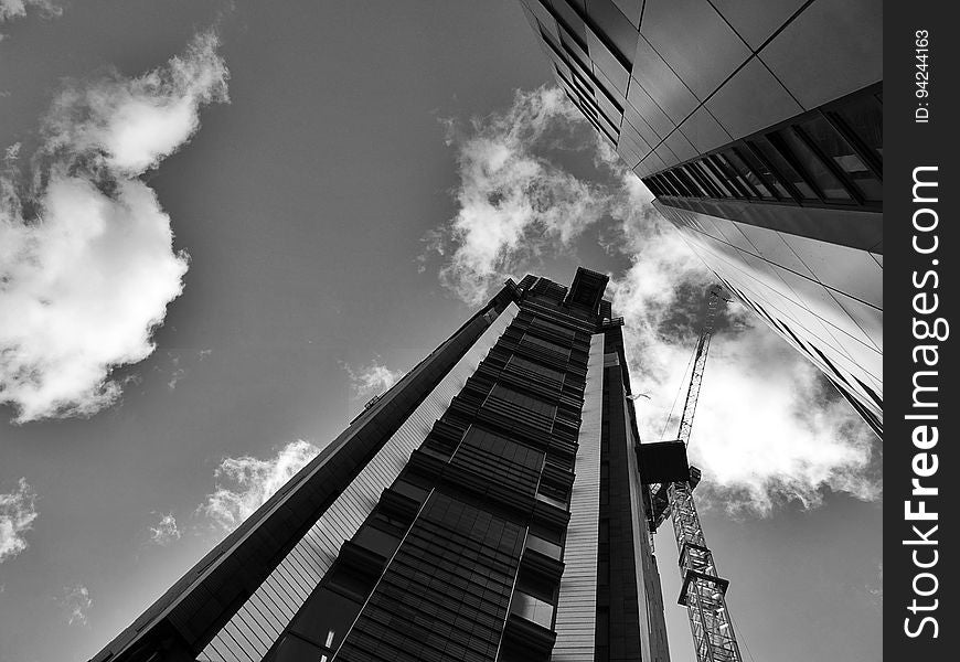 High rise building under construction with crane against cloudy skies in black and white. High rise building under construction with crane against cloudy skies in black and white.