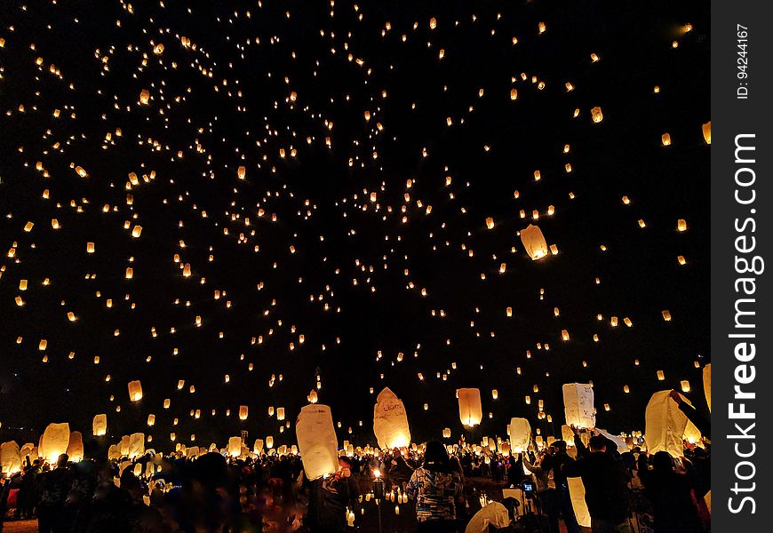 A crowd of people at a celebration and sky lanterns floating in the air.