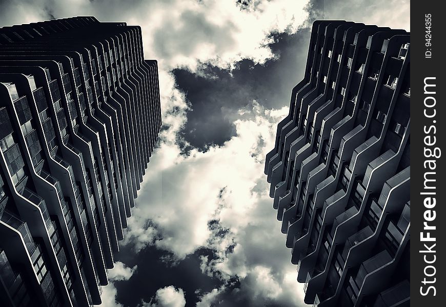 Two high rise buildings, comprising apartments constructed from steel, concrete and glass, with staggered balconies creating an unusual abstract pattern, monochrome with sky and white clouds. Two high rise buildings, comprising apartments constructed from steel, concrete and glass, with staggered balconies creating an unusual abstract pattern, monochrome with sky and white clouds.