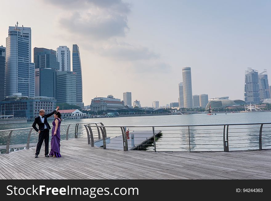 Couple in evening dress on a jetty or riverside decking about to dance, background of river and skyscrapers. Couple in evening dress on a jetty or riverside decking about to dance, background of river and skyscrapers.