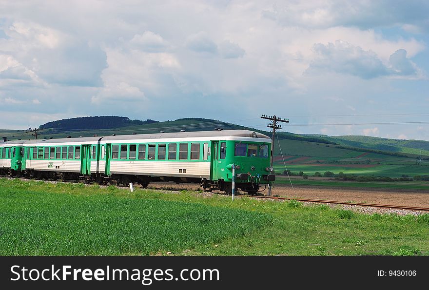 Green passenger train moving through the hills