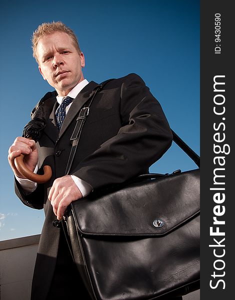 A businessman holding a briefcase and umbrella outside. A businessman holding a briefcase and umbrella outside