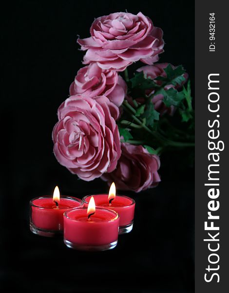 Three lit candles with some pink flowers. Three lit candles with some pink flowers