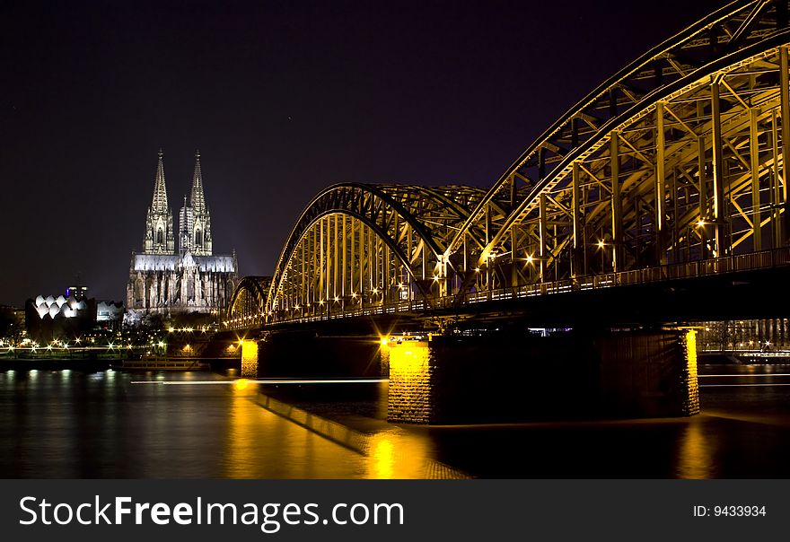 Dom and Hohenzollern bridge in Cologne at night lighting with reflection in river Rhine.