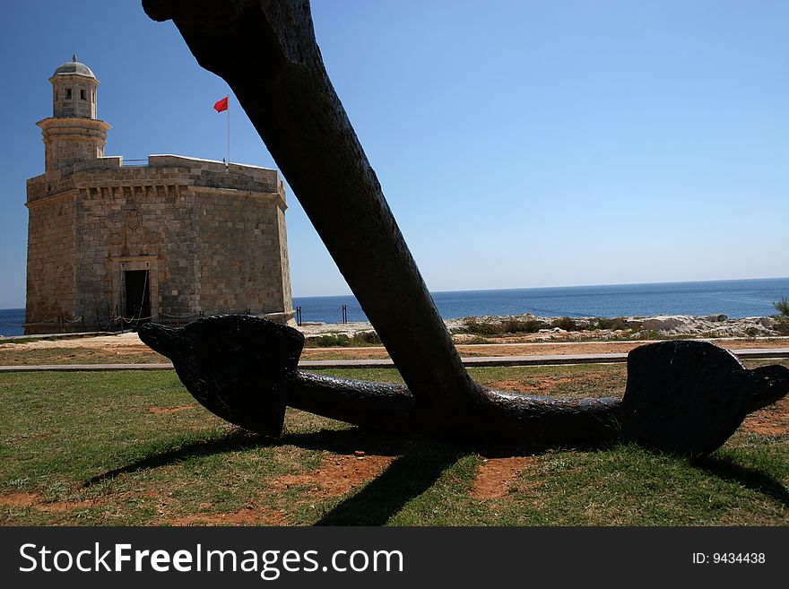 Anchor with a fortress in a background on a coast. Anchor with a fortress in a background on a coast