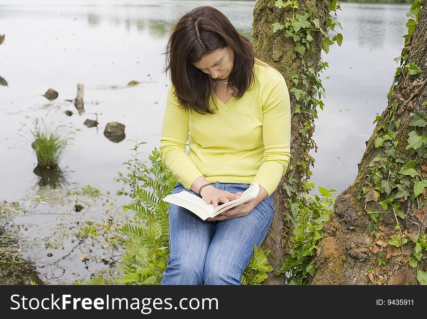 A young woman reading a book sited on a park