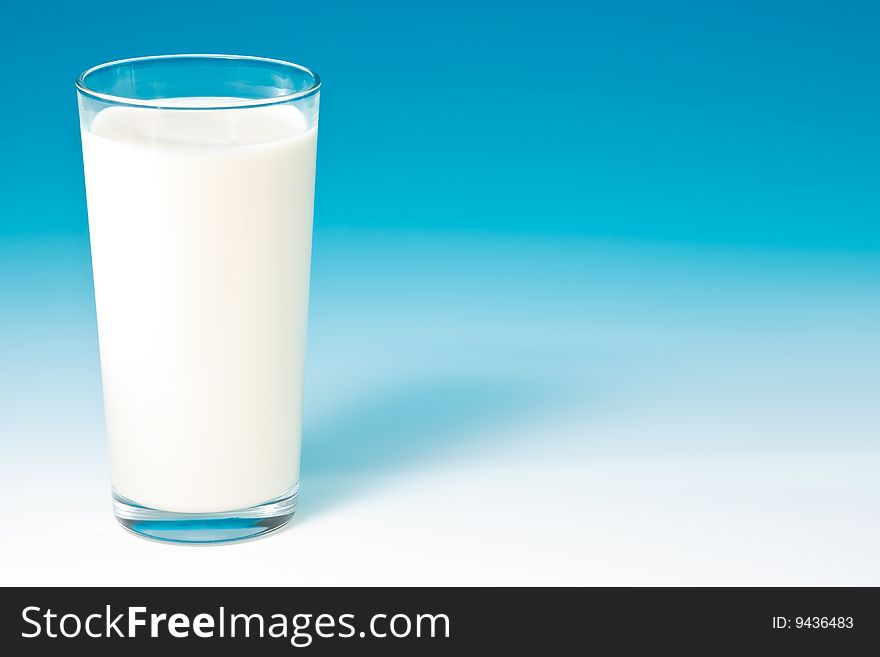 Cool fresh milk in a tall glass on blue gradient studio background.  with copy space