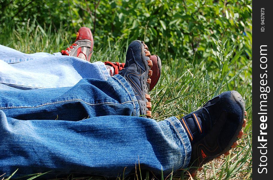 Two people wearing jeans and running shoes laying in the green grass. Two people wearing jeans and running shoes laying in the green grass