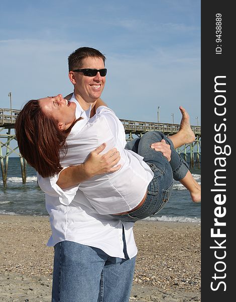 A young couple enjoying time together at the beach.  The man is holding the woman in his arms and they are both laughing. A young couple enjoying time together at the beach.  The man is holding the woman in his arms and they are both laughing.