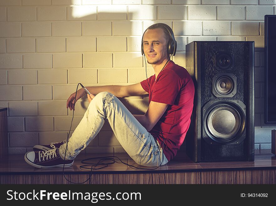 Handsome man, a music lover listens to music with headphones with a mobile phone in a modern interior against the media and large speakers. Enjoying music is fun and communicates on the Internet at home. The concept of creative and positive lifestyle. Handsome man, a music lover listens to music with headphones with a mobile phone in a modern interior against the media and large speakers. Enjoying music is fun and communicates on the Internet at home. The concept of creative and positive lifestyle