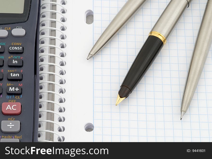 Spiral notebook with blue grid. Calculator, pen, pencil and fountain pen. Selective focus