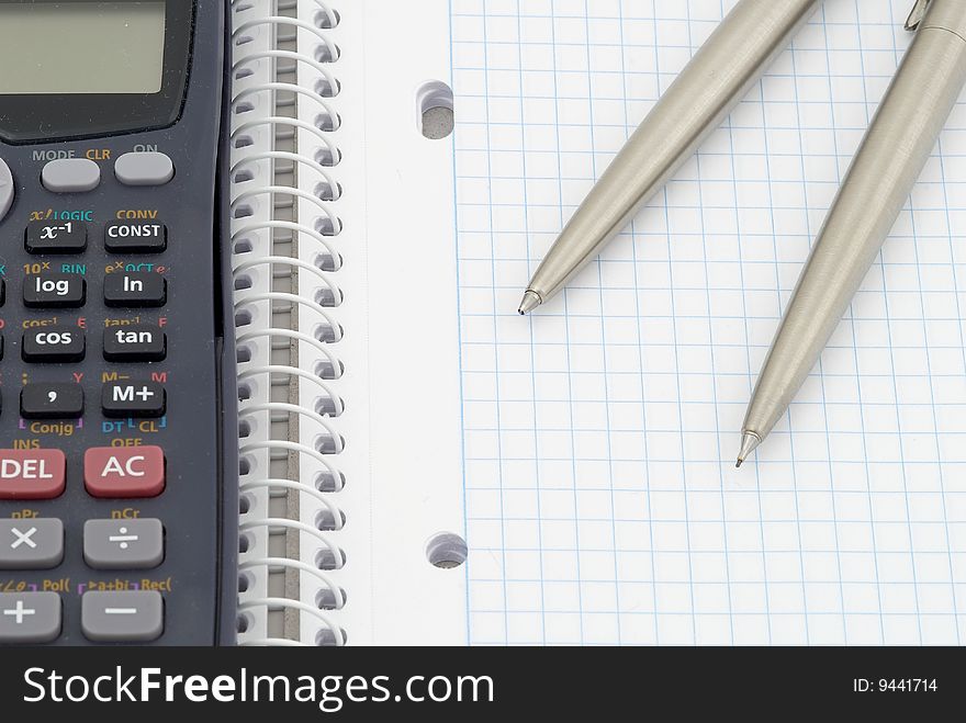 Spiral notebook with blue grid. Calculator, pen and  pencil. Selective focus