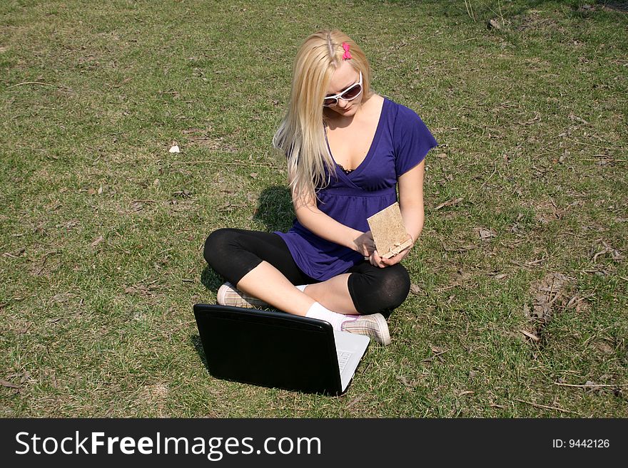 Studying girl with a laptop and copybook sitting on grass