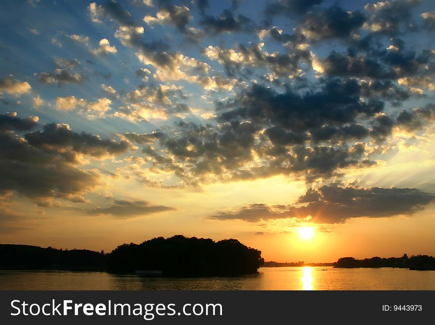 A bright sunset in a still evening deep in a high cloudy sky behind the river