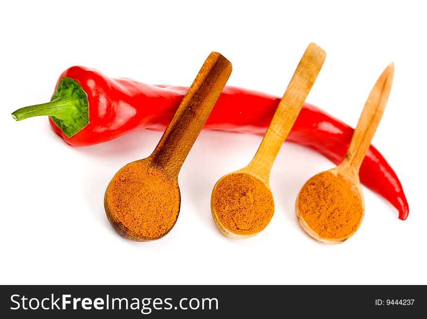 A composition of a pod of red chile pepper and three wooden spoonful of red ground pepper on a white background. A composition of a pod of red chile pepper and three wooden spoonful of red ground pepper on a white background