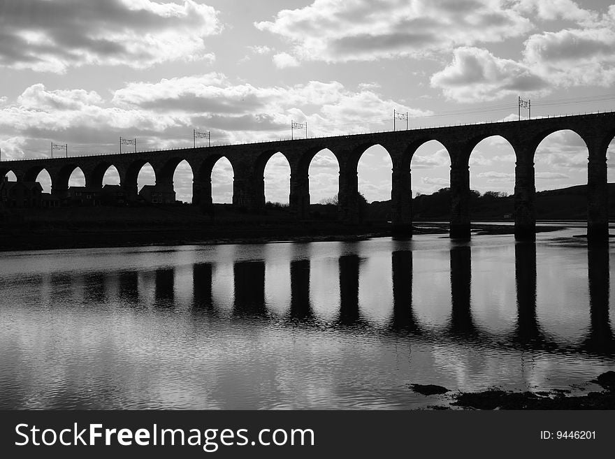 Wide black and white shot of the Royal Border Railway Bridge at Berwick Upon Tweed, taken as a silhoutte against a semi cloudy sky with the bridge reflecting in the water. Wide black and white shot of the Royal Border Railway Bridge at Berwick Upon Tweed, taken as a silhoutte against a semi cloudy sky with the bridge reflecting in the water.