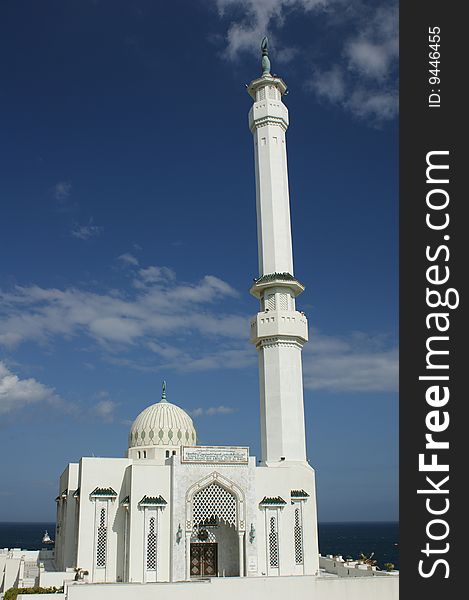 White marble mosque on the coast of Gibraltar, under a blue sky with the sea in the background.