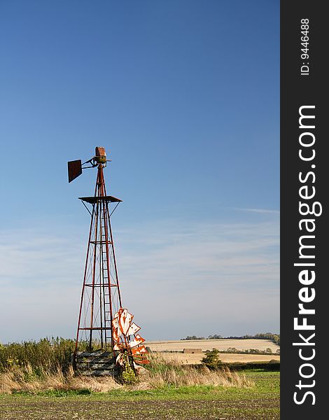 A derelict prairie windmill in a field under a blue sky.