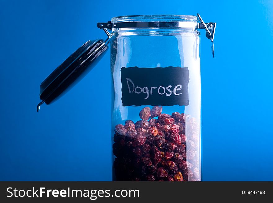 Inscription Dogrose on transparent glass jar. Over blue background