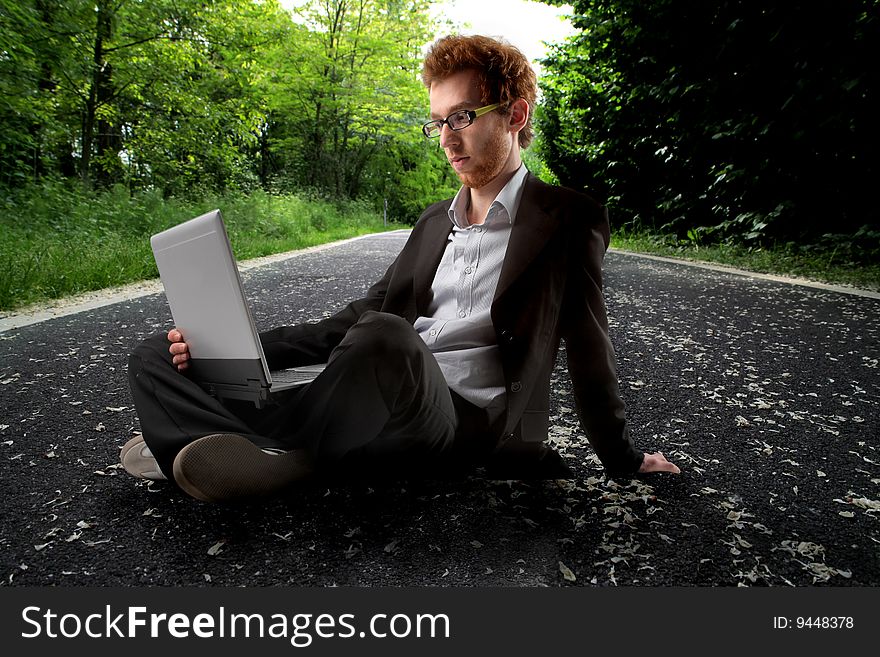 Young man in formal suit using laptop on a country road. Young man in formal suit using laptop on a country road