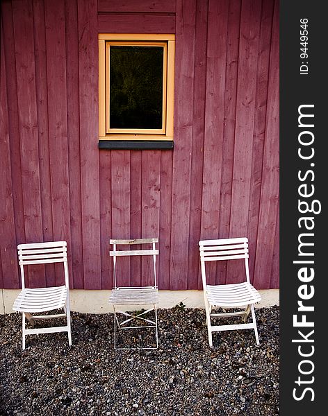 Three white chairs against a red house