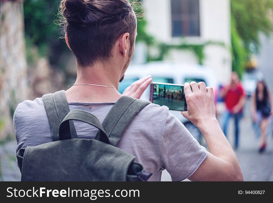 Man traveler makes a photo on your smartphone on a city street. The concept of connection and communication in the journey. Man traveler makes a photo on your smartphone on a city street. The concept of connection and communication in the journey.