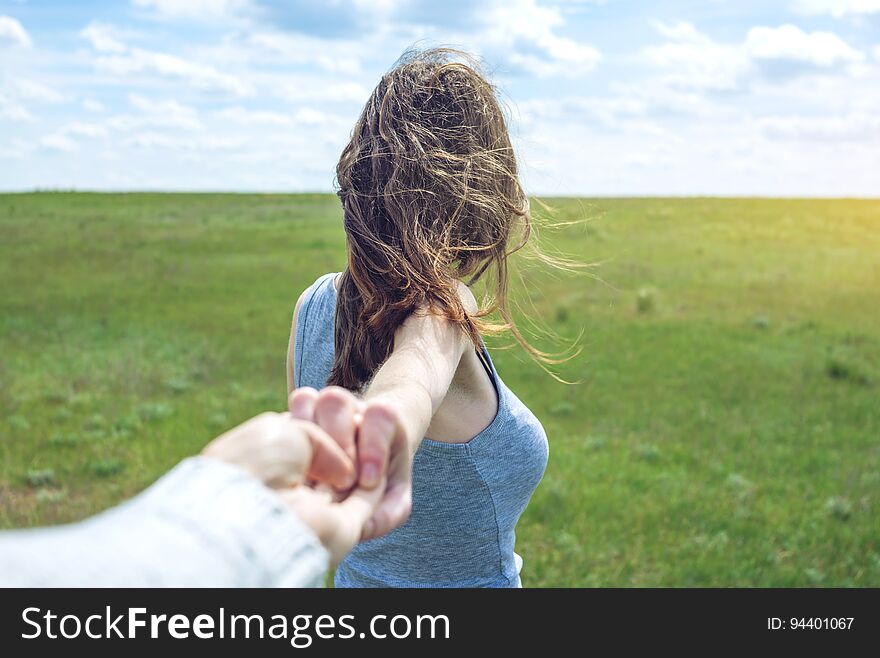 Follow me, Attractive brunette girl holding the hand of the leads in a clean green field, steppe with clouds