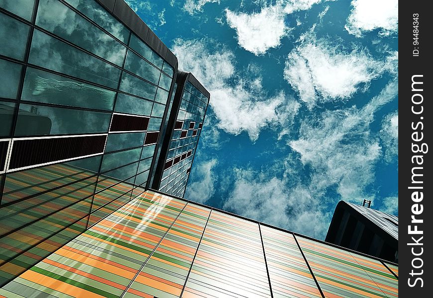 Facade of architecturally designed buildings with one wall in banded pastel colors, reflected in a second glass wall, blue sky and cloud above. Facade of architecturally designed buildings with one wall in banded pastel colors, reflected in a second glass wall, blue sky and cloud above.