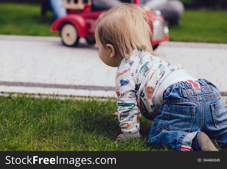 Toddler crawling through green grass toward red toy truck. Toddler crawling through green grass toward red toy truck.