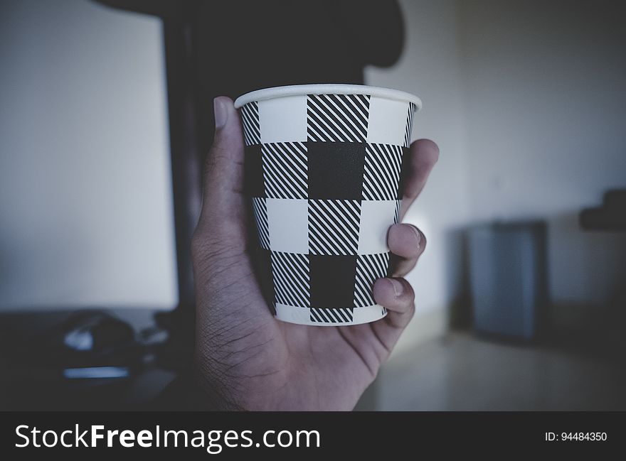 Close up of hand holding brown and white plaid disposable hot beverage cup. Close up of hand holding brown and white plaid disposable hot beverage cup.