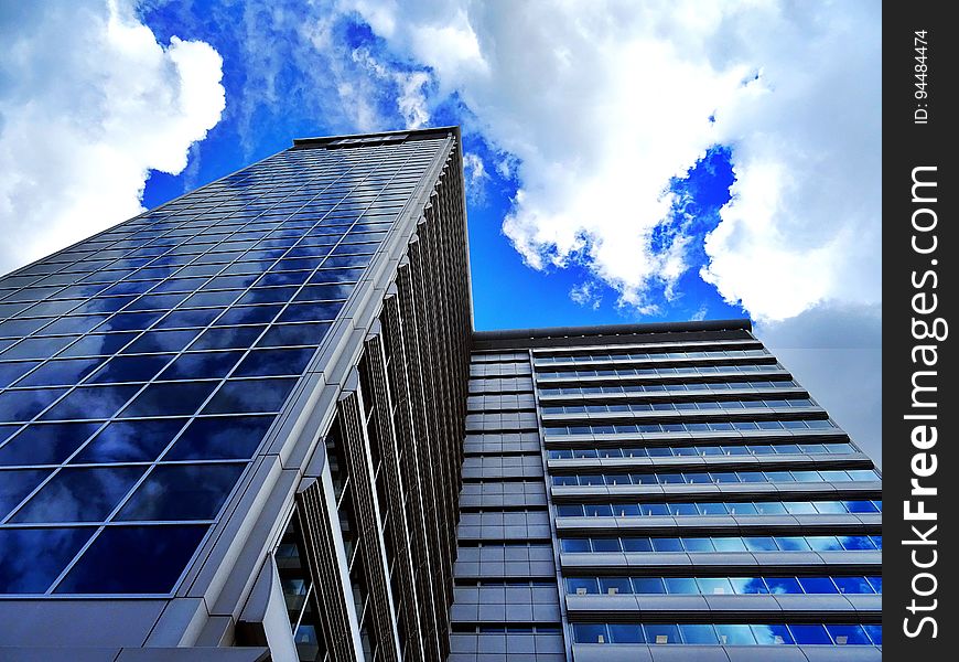 Skyscraper building with L-shaped facade (staggered) viewed at an acute angle with blue sky and cloud reflections in the windows. Skyscraper building with L-shaped facade (staggered) viewed at an acute angle with blue sky and cloud reflections in the windows.