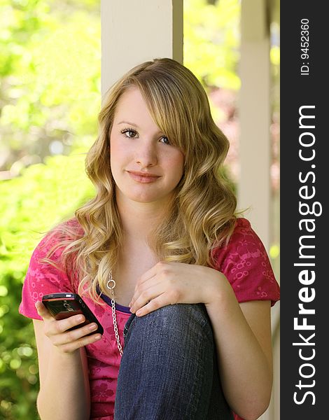 Attractive teenager sitting on front porch calling friend wearing pink