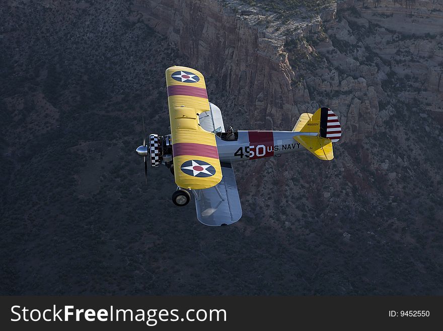 Yellow 1942 steerman flying over large rock canyon. Yellow 1942 steerman flying over large rock canyon.